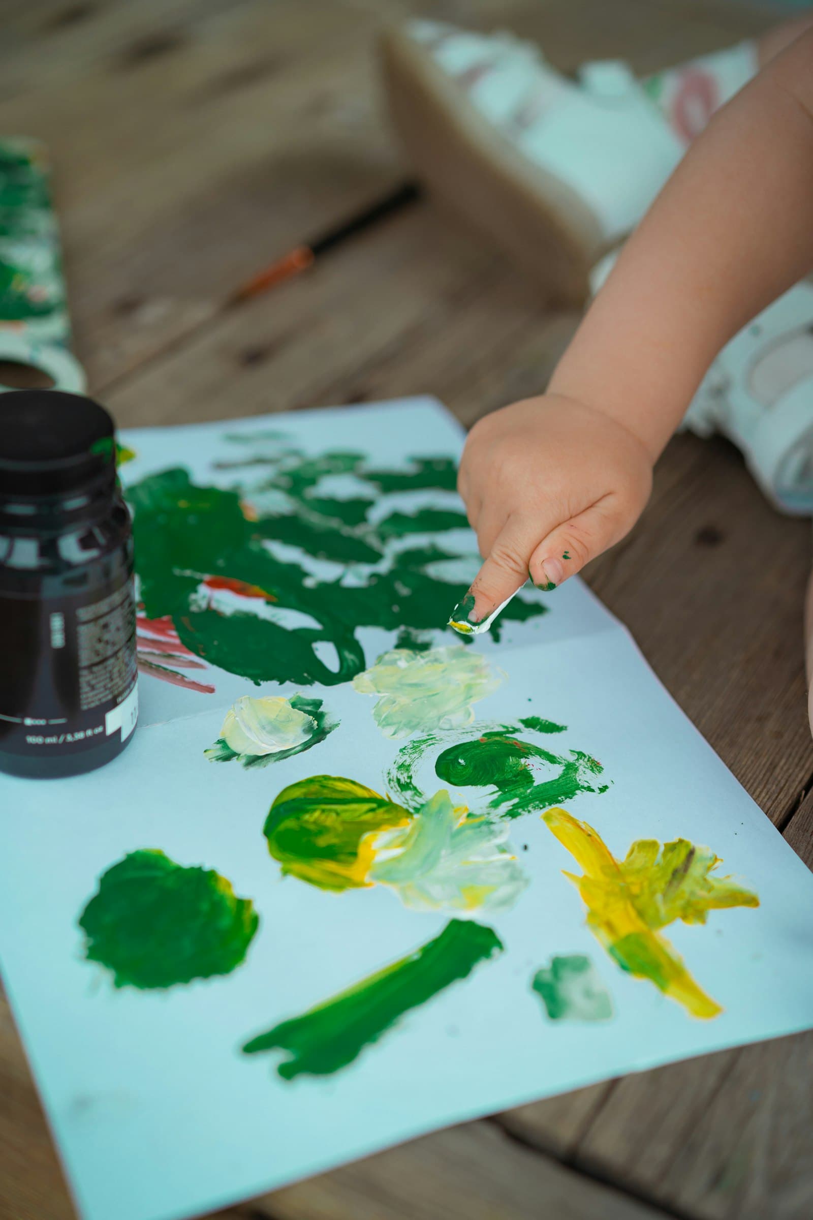 Toddler painting on a piece of paper at a craft table